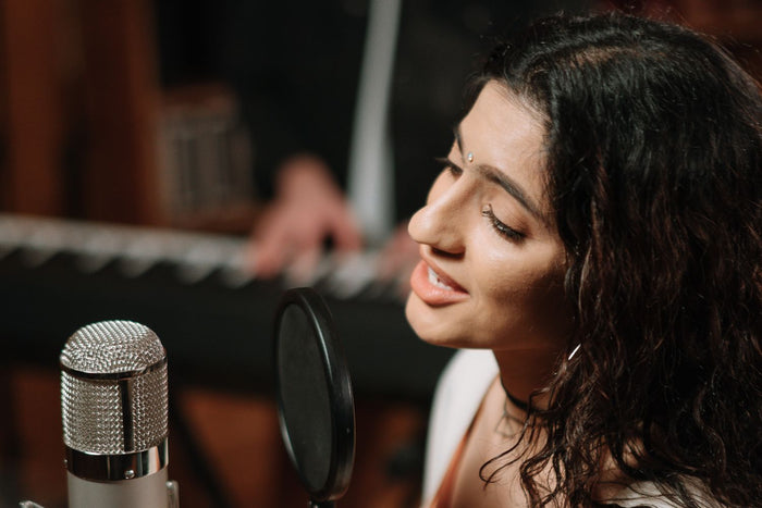 Vocalist singing into a microphone in a recording studio booth