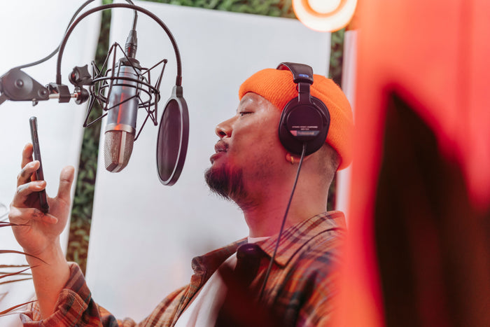 Producer at mixing console with artist visible in recording booth through glass