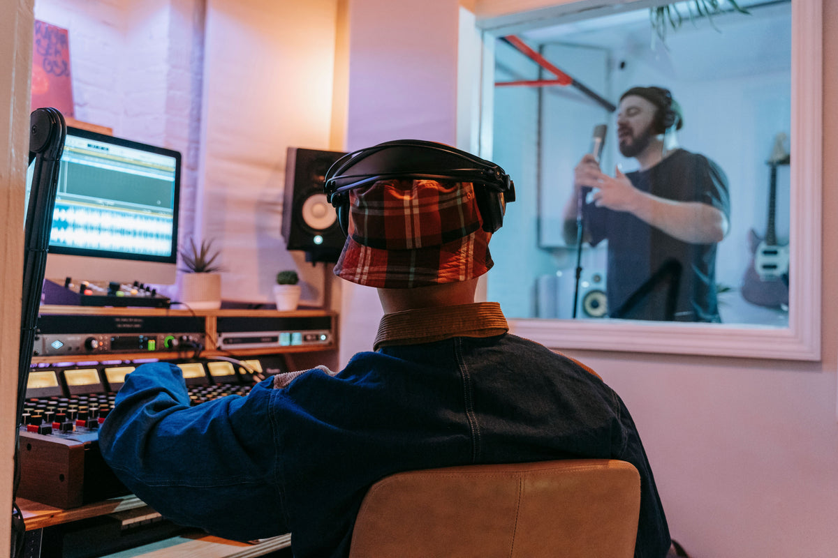 Producer at board while artist performs in studio booth generating real music income